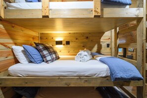 Ein Stockbett mit Holzkopfstütze, weißer Bettwäsche und einem kleinen Wandheizgerät.