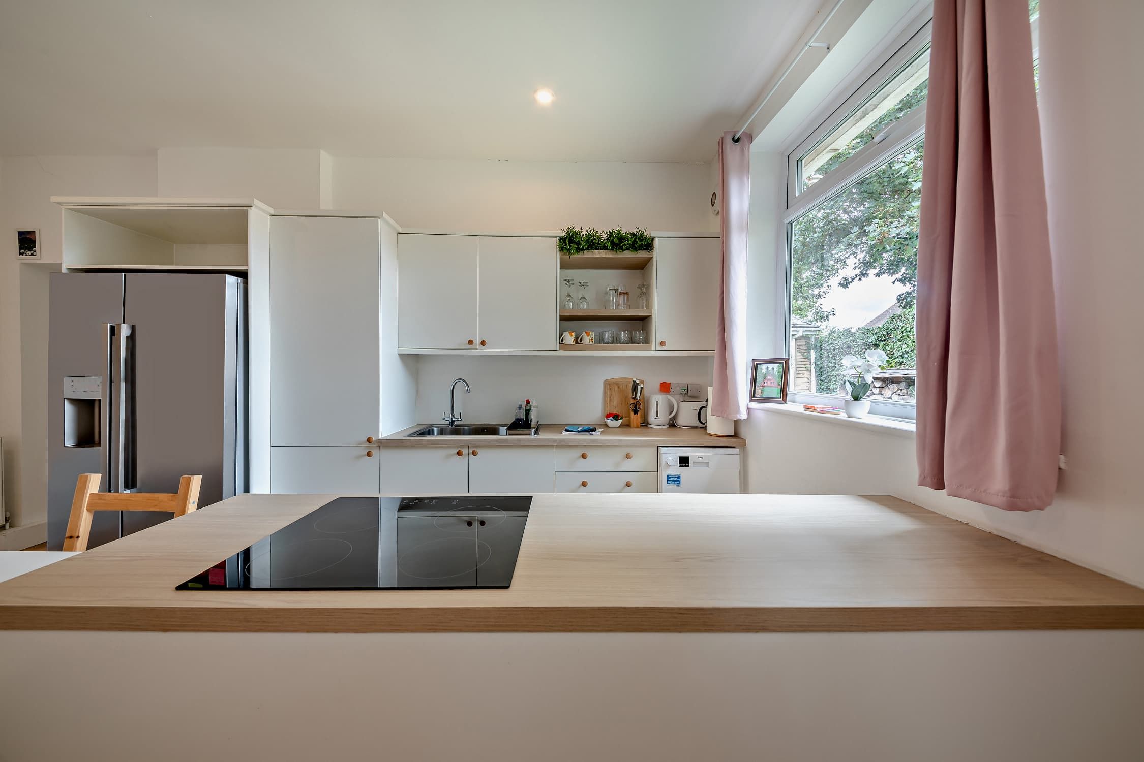 Une cuisine moderne avec une table à manger, des appareils électroménagers intégrés et une fenêtre avec des rideaux.