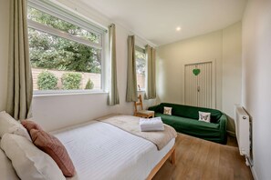 A bedroom with a bed, a green sofa, a window with curtains, and a door with a heart-shaped decoration.