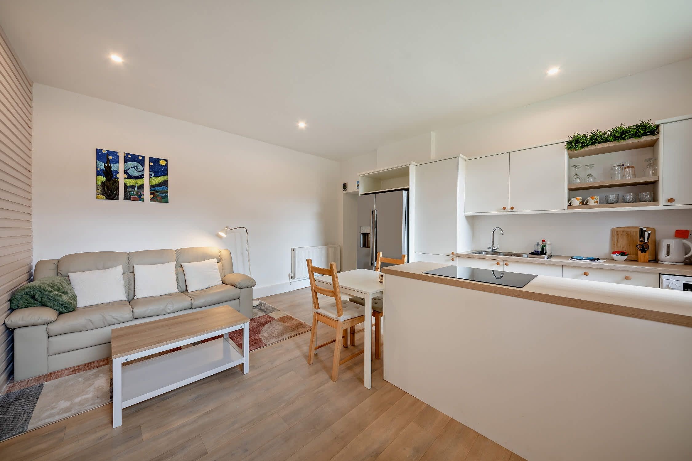 A modern kitchen with a central island, white cabinetry, and a dining area with a sofa and table.