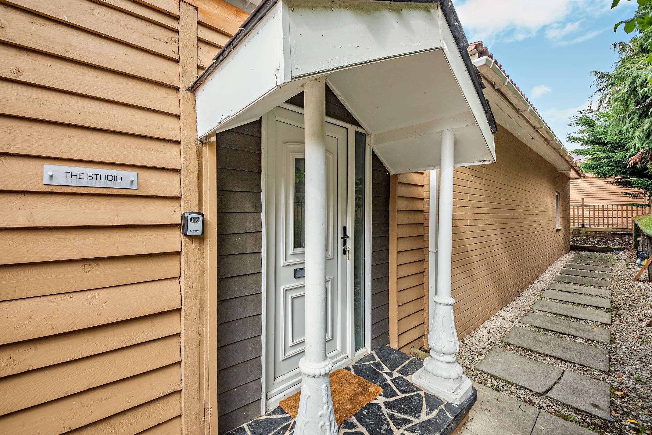 Un bâtiment en bois avec une enseigne indiquant « THE STUDIO » et une porte surmontée d’un petit porche blanc.