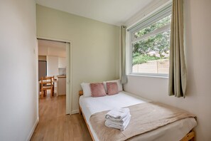 Ein Schlafzimmer mit einem Bett, einem Fenster mit Vorhängen, einer kleinen Küchenzeile und einem Holzboden.