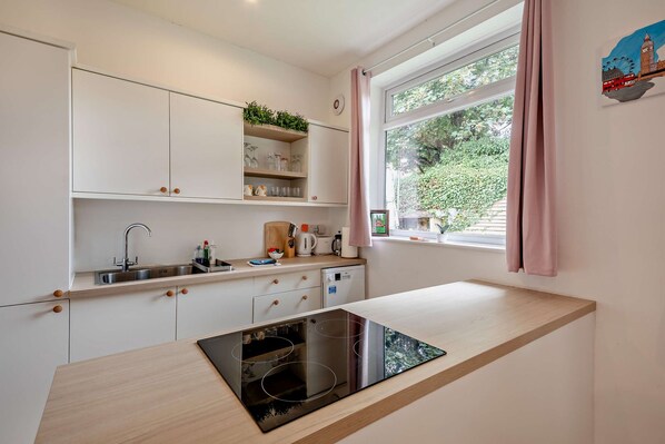 A modern kitchen with white cabinets, a built-in dishwasher, and a window with a view of greenery.