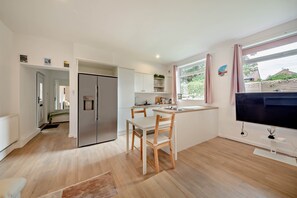 A modern kitchen with a built-in fridge, wooden chairs, a dining table, and a large window with curtains.