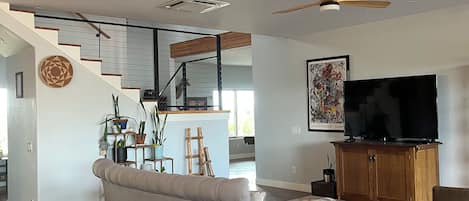 A modern living room with a sofa, a television, and a staircase leading to an upper level.