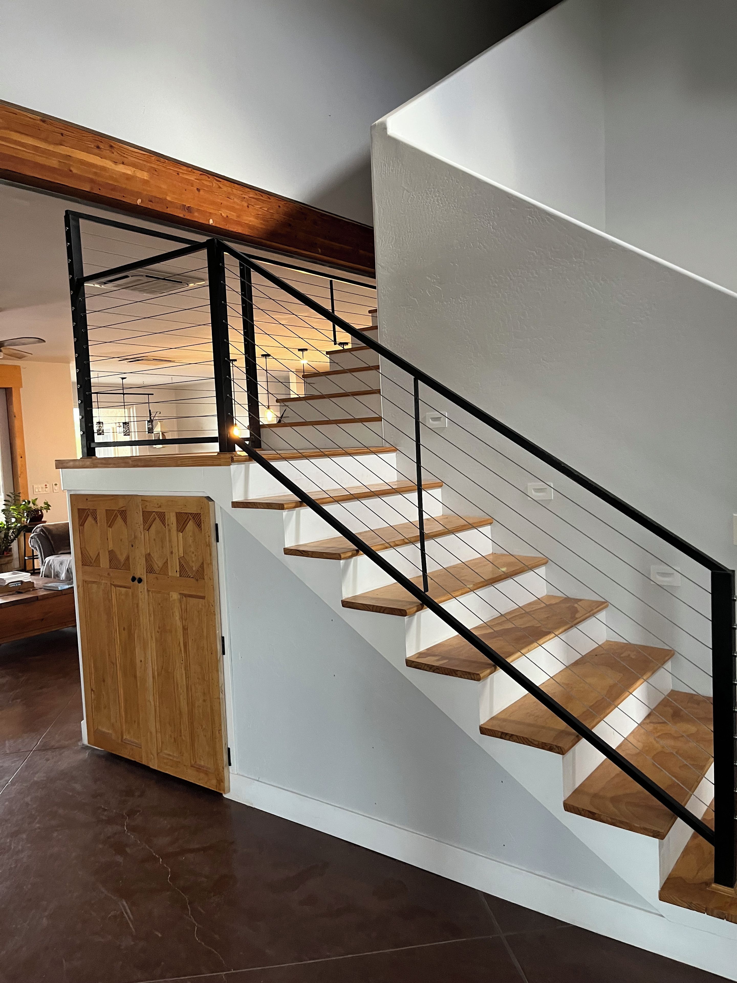 A staircase with wooden steps and a black railing, leading to a landing with a wooden door.
