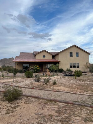 A two-story house with a red roof, beige exterior, and a front porch with outdoor furniture.