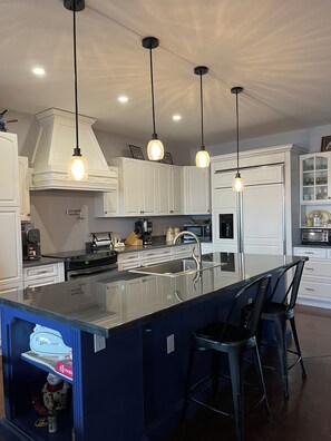 A modern kitchen with white cabinetry, a central island with bar stools, pendant lighting, and a built-in oven.