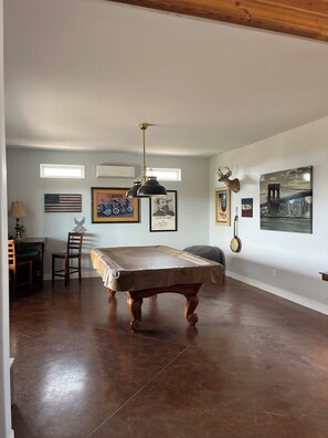 A spacious room with a pool table, a ceiling fan, and various wall decorations including framed pictures and a mounted animal head.
