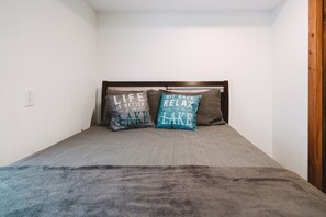 A single bed with two pillows, a wooden headboard, and a plain white wall with a power outlet.