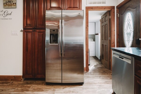 A stainless steel refrigerator with a water dispenser, wooden cabinets, and a Bosch dishwasher in a kitchen with a wooden floor.