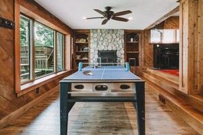 A ping pong table in a room with wooden walls, a stone fireplace, and a ceiling fan.