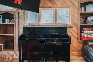 A room with a piano, wooden walls, and a window with blinds. - Long Lake Extended-Stay Furnished 30-Day+ Home (Ingleside)