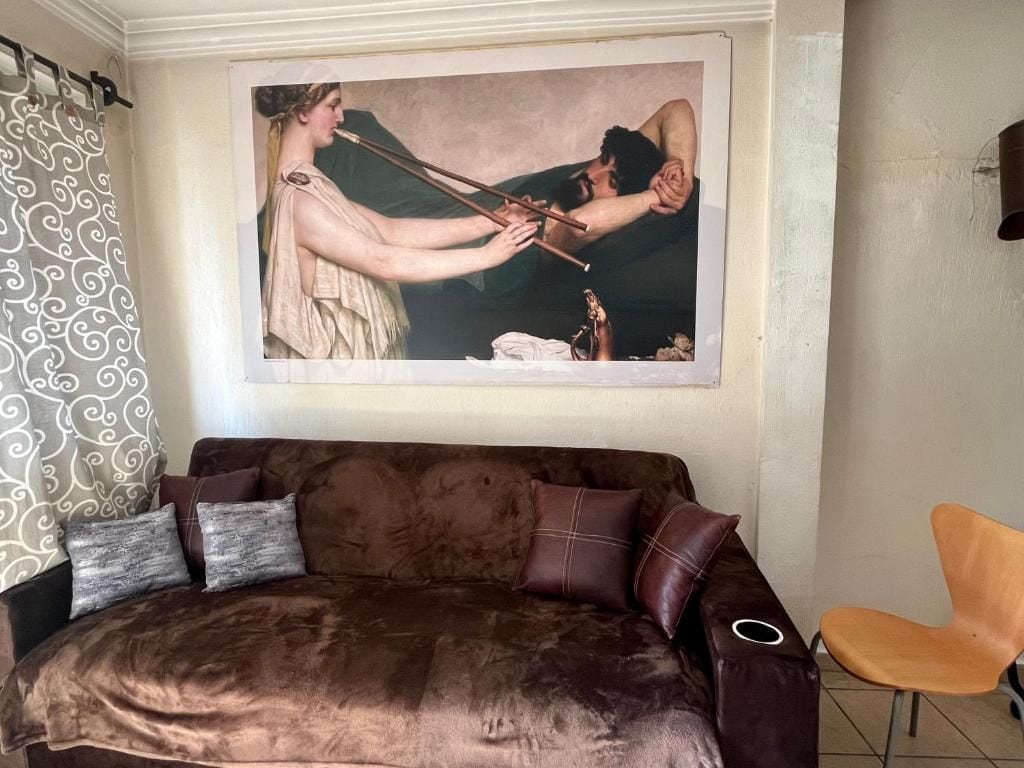 A room with a brown sofa, a chair, and a large painting on the wall.