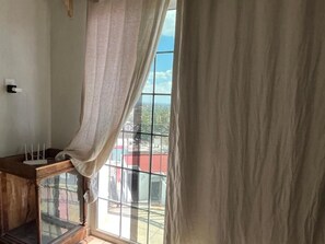 Huoneessa on suuri ikkuna, lasikantisella yläosalla varustettu puinen kaappi ja pistorasia seinässä.