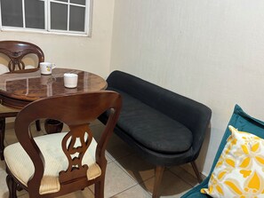 A dining area with a round table, chairs, a sofa, and a window.