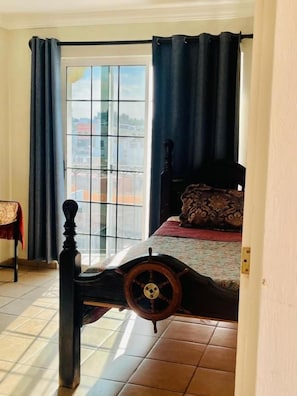 Una habitación con una cama que destaca por su cabecera decorativa en forma de rueda, una ventana con cortinas y vistas a la ciudad.