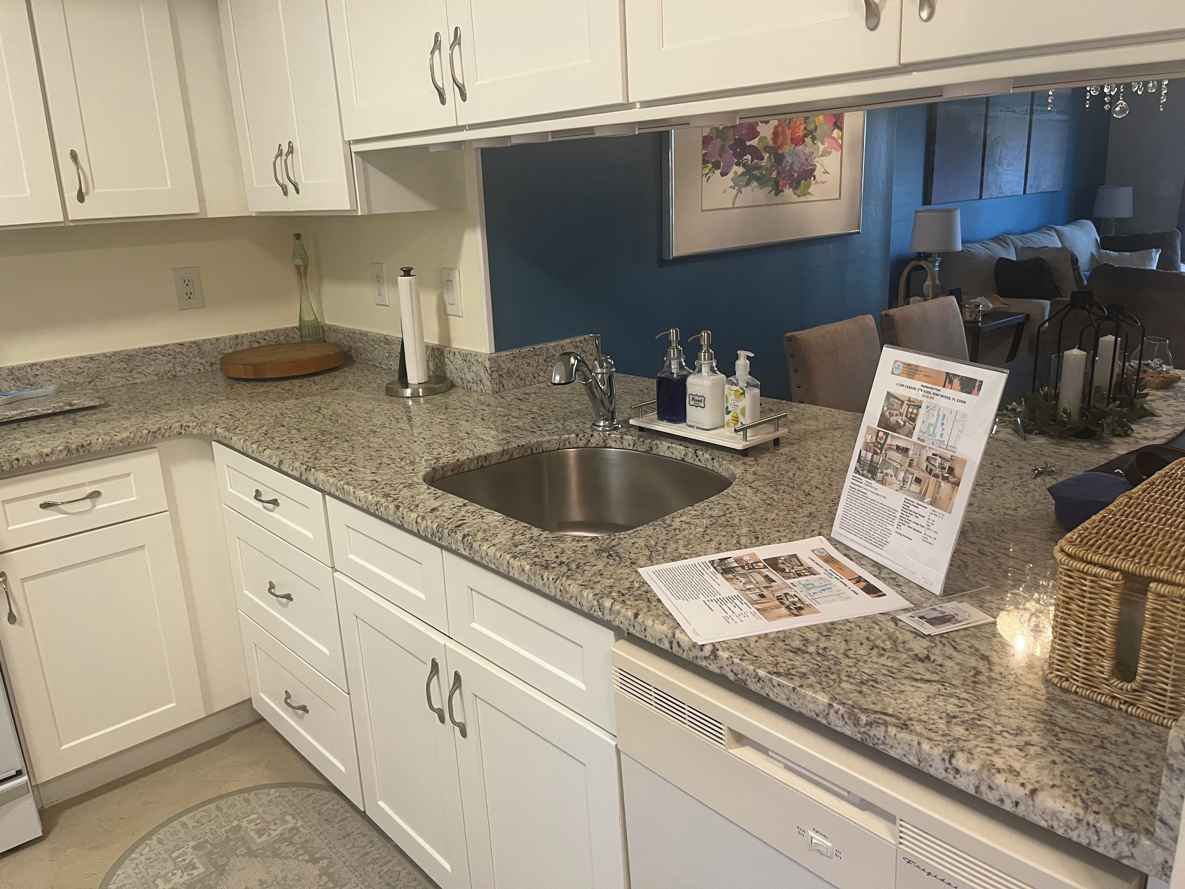 A kitchen with white cabinets, a granite countertop, a stainless steel sink, and a dining area with a table and chairs.