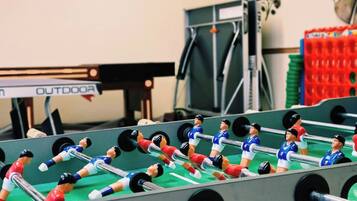 Een tafelvoetbaltafel met meerdere spelers en een pingpongtafel op de achtergrond.
