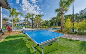 Ein gut gepflegter Außenbereich mit Tischtennisplatte, Palmen und blauem Himmel.