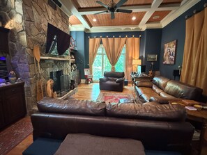 A living room with a stone fireplace, leather sofas, a flat-screen TV, and a ceiling fan. - Secluded Lake Norman Waterfront Luxury, 4BR, 5.5 Baths with Home Theater (Mooresville)