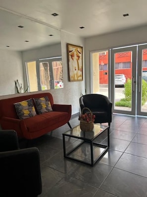 A modern living area with a red sofa, a black armchair, and a glass coffee table. - Hotel Capri (Iquique)