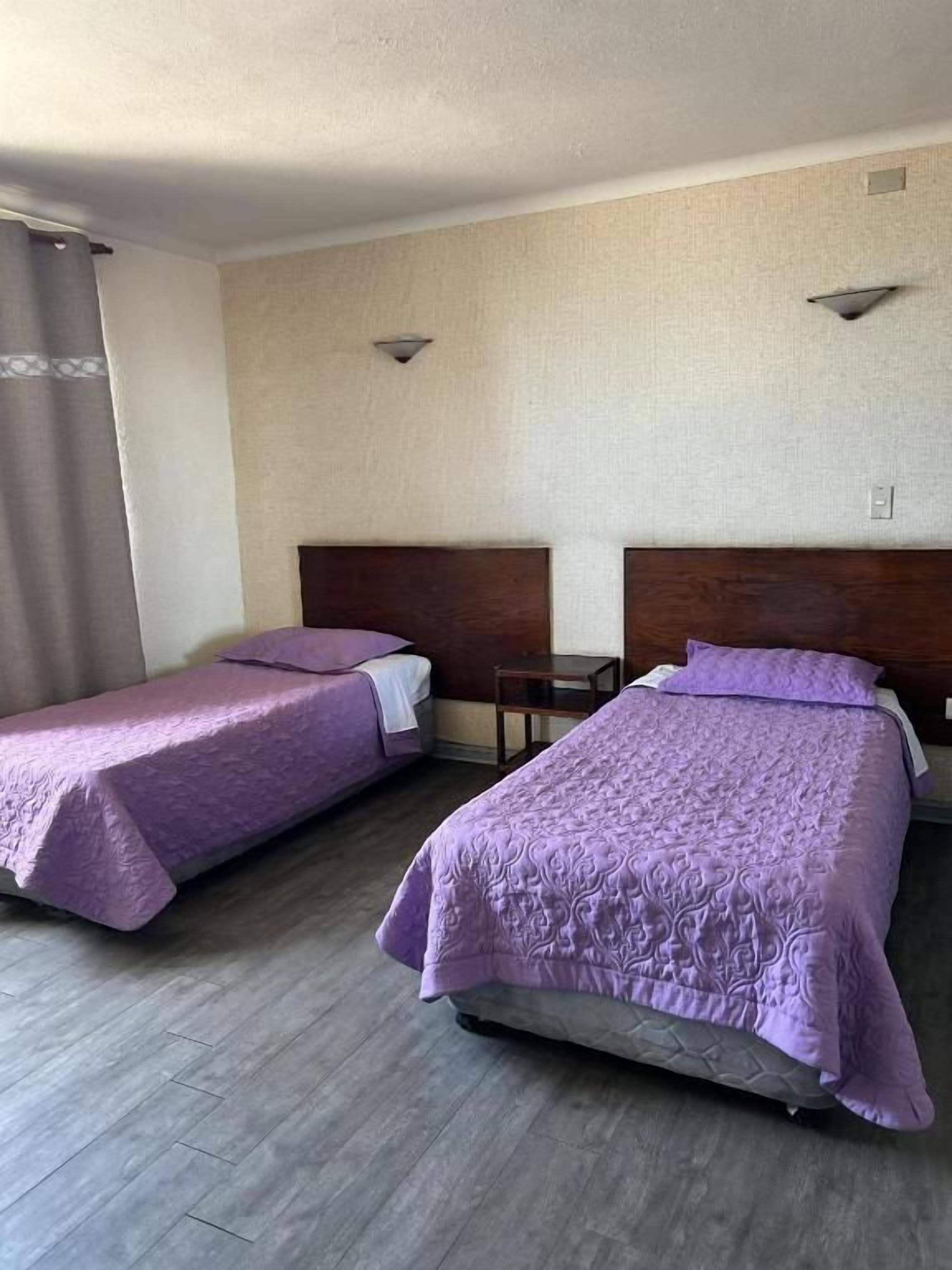 Habitación de hotel con dos camas, una mesita pequeña y una silla.