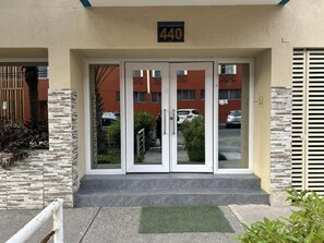 A building entrance with a double door, a number sign above, and a small green mat at the entrance. - Hotel Capri (Iquique)