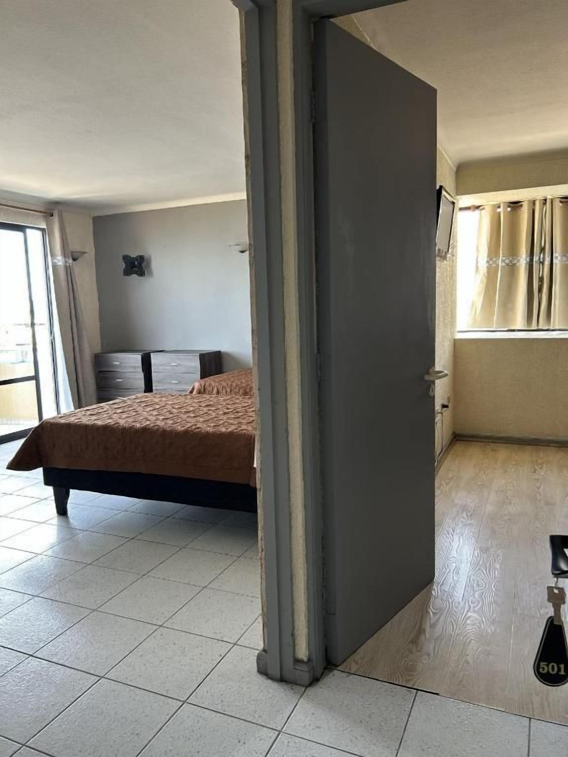 Una habitación con cama, armario y ventana con cortinas.
