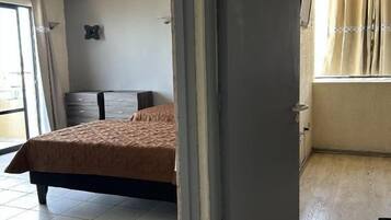 Una habitación con cama, armario y ventana con cortinas.