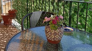 Un tavolo rotondo con un vaso di fiori su un balcone affacciato su una collina.