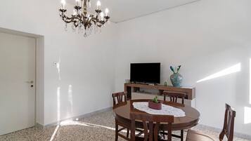 A dining area with a round table, chairs, a chandelier, a flat-screen TV, and a decorative vase.