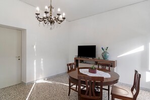 Un comedor con una mesa redonda, sillas, una araña, un televisor de pantalla plana y un jarrón decorativo.