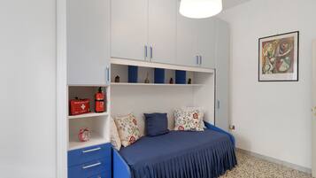 Una camera da letto con un letto, cassetti, una mensola con oggetti e un quadro appeso al muro.