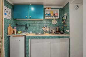 Eine Küche mit türkis-gefliestem Fliesenspiegel, einem weißen Kühlschrank, einer Kaffeemaschine und diversen Küchenutensilien.
