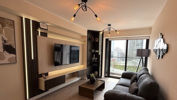 A modern living room with a flat-screen TV, a sofa, a coffee table, and a bookshelf. - Aparts4Days Gym, Pool, and Jacuzzi 1-Bedroom Apartment (San Isidro)