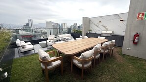 A rooftop terrace with a wooden table and chairs, a fire extinguisher, and a city view. - Aparts4Days Gym, Pool, and Jacuzzi 1-Bedroom Apartment (San Isidro)