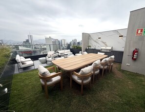 En takterrass med ett träbord och stolar, en brandsläckare och utsikt över staden.