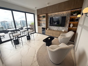A modern living room with a large TV, comfortable seating, a dining area, and a view of the cityscape. - Aparts4Days Fitness, Pool, and Jacuzzi 1-Bedroom Apartment (San Isidro)