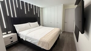 A bedroom with a bed, bedside tables, a wardrobe, and a TV. - Aparts4Days Gym, Pool, and Jacuzzi 1-Bedroom Apartment (San Isidro)