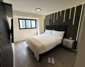 A modern bedroom with a large bed, bedside tables, a window, and a view of buildings outside. - Aparts4Days Gym, Pool, and Jacuzzi 1-Bedroom Apartment (San Isidro)