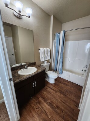 Un baño con tocador, lavamanos, espejo, inodoro y bañera.