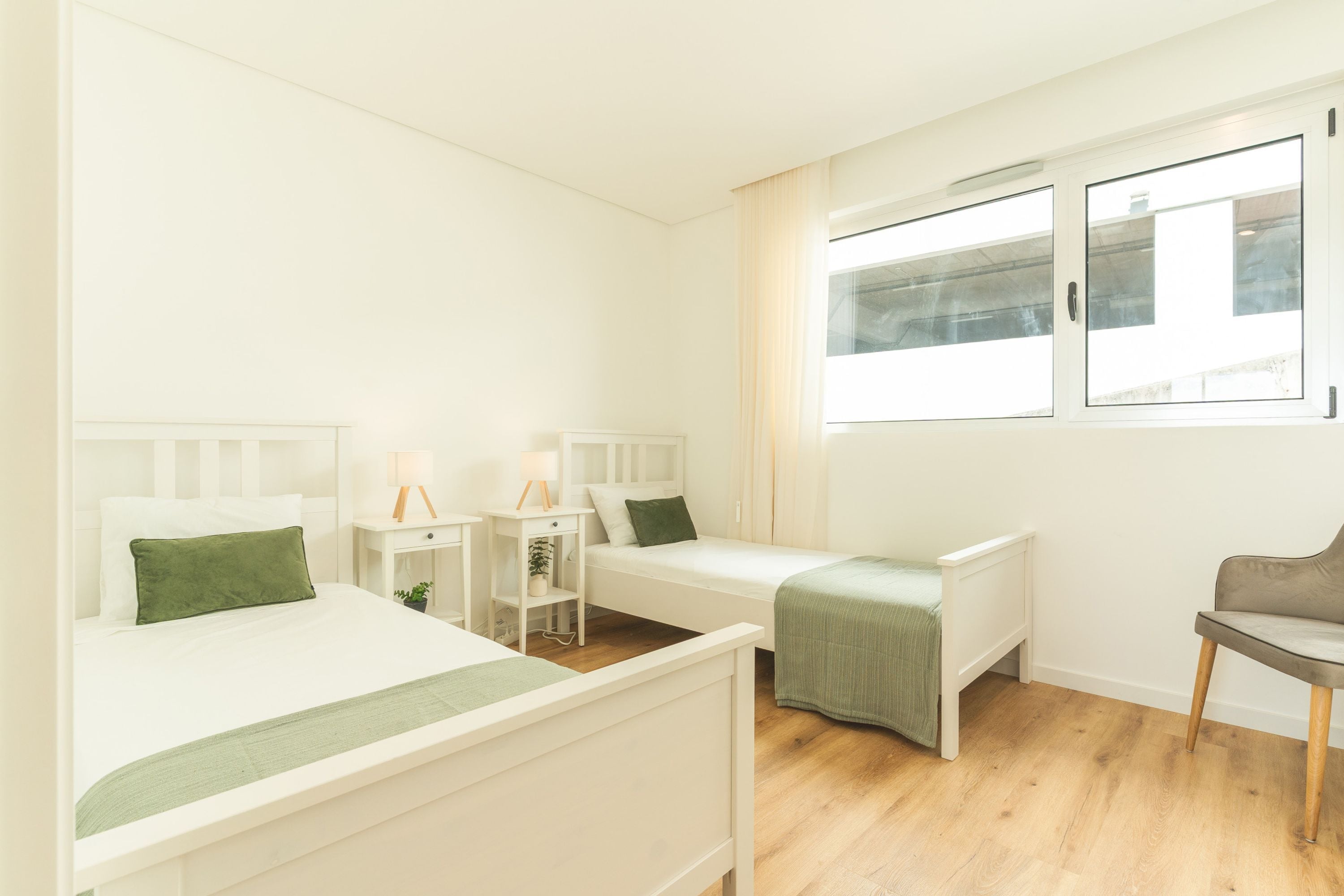 Habitación de hotel con dos camas individuales, un escritorio pequeño, una silla y ventana con vistas.