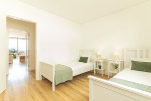 A minimalist bedroom with two single beds, a small bedside table with a lamp, and a view of an outdoor balcony. - Sunny Stay Atlantic Gardens by Atlantic Holiday (Camara de Lobos)