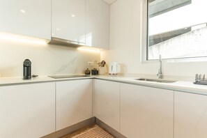 A modern kitchen with white cabinetry, a built-in stove, a coffee maker, and a window with a view. - Sunny Stay Atlantic Gardens by Atlantic Holiday (Camara de Lobos)