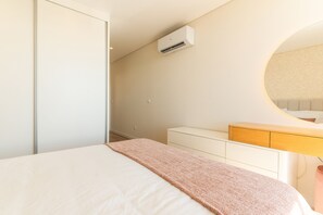Ein Schlafzimmer mit Bett, Nachttisch, Kommode, Spiegel und Klimaanlage.