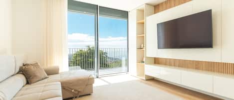 A modern living room with a sofa, a flat-screen TV mounted on the wall, and a sliding glass door leading to a balcony.