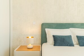 A neatly made bed with white and teal pillows, a bedside lamp, and a textured wall. - Sunny Stay Atlantic Gardens by Atlantic Holiday (Camara de Lobos)
