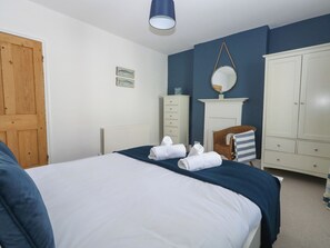 A bedroom with a bed, a dresser, a mirror, and a door. - Quarry Cottage (Portland)