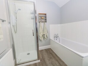 A bathroom with a glass-enclosed shower, a bathtub, and a shelf with towels. - Quarry Cottage (Portland)